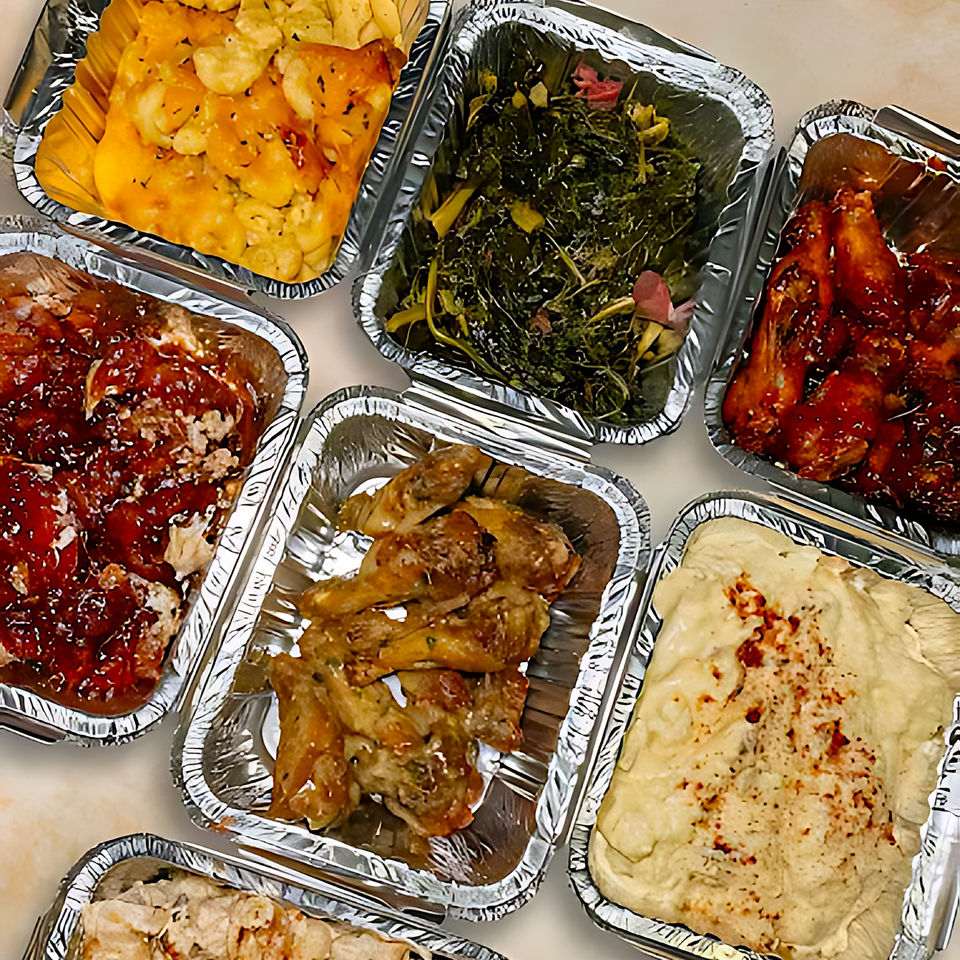 Assortment of soul food dishes in foil containers, including mac and cheese, collard greens, and chicken.